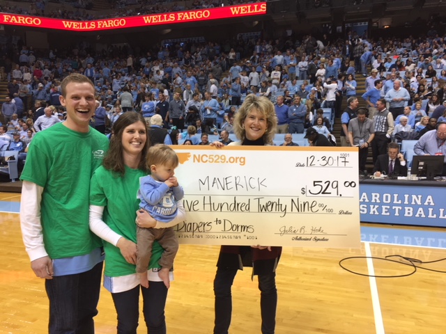 11-month-old Maverick Steele with his parents Andrew and Taylor Steele stand next to a check for $529 at the Wake Forest versus University of North Carolina men's basketball game.